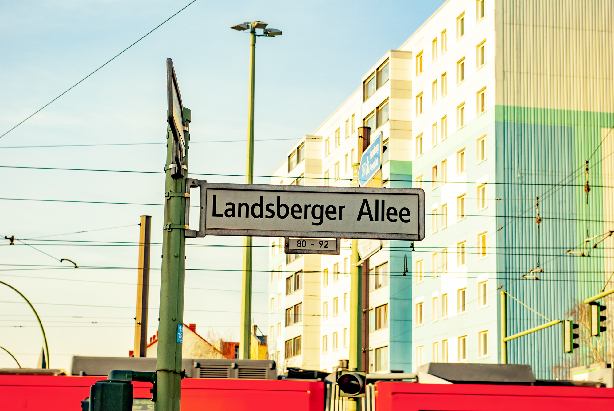 Schild mit dem Straßennamen Landsberger Allee. Im Hintergrund steht ein Hochhaus im Plattenbaustil.