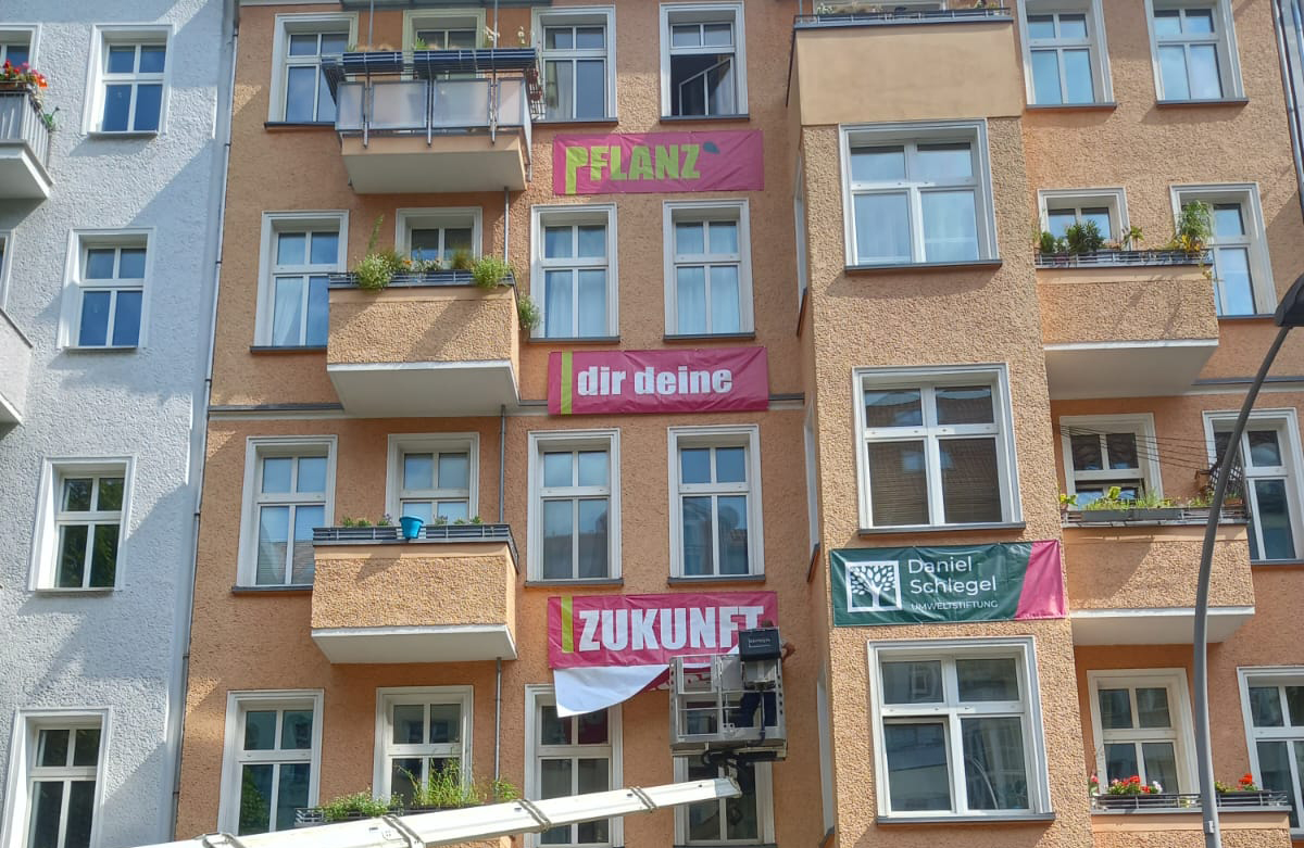 Umweltbotschaften an einer terrakottafarbenen Hausfassade mit drei Werbeplanen auf denen steht:"Pflanz Dir Deine Zukunft".
